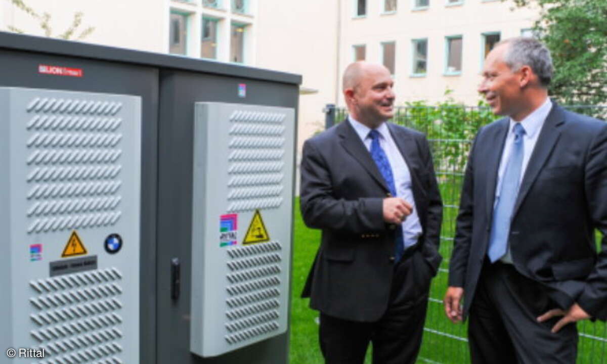 Was nicht verbraucht wird, speichern die Hochleistungsbatterien im Inneren des Rittal-Schrankes - erst dann wird ins öffentliche Stromnetz eingespeist. Staatssekretär Rainer Bomba (links) und Dr. Julian Weber, Leiter Innovationsprojekte bei der BMW G