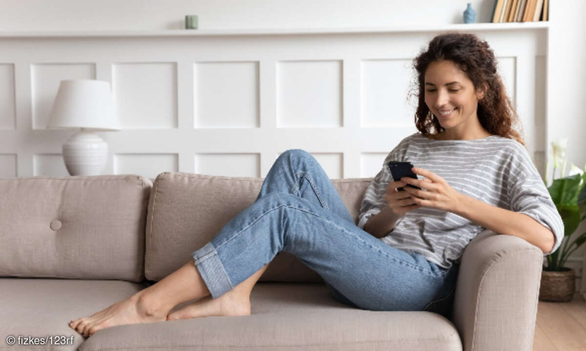 Lächelnde Frau mit Smartphone auf Sofa