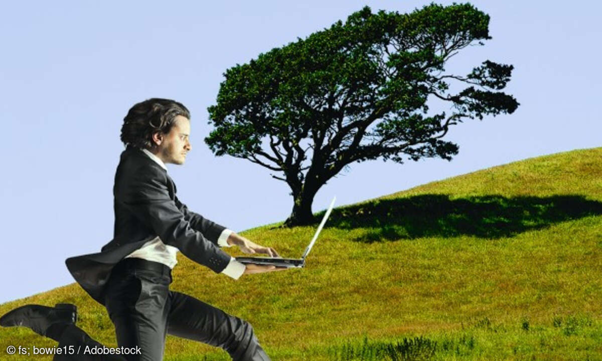 Mann mit Laptop rennt auf einer Wiese