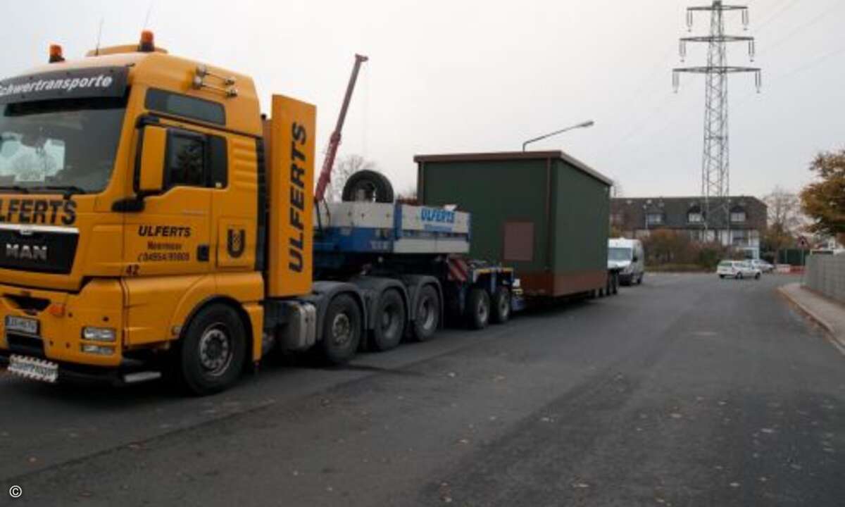 Gegen acht Uhr morgens wird der PoP vom Hersteller schon fertig zur Aufstellung auf einem Schwerlast-Tieflader angeliefert. Gleichzeitig wird der Mobilkran mit Kontergewichten bestückt. (Foto: KomMITT Ratingen GmbH)