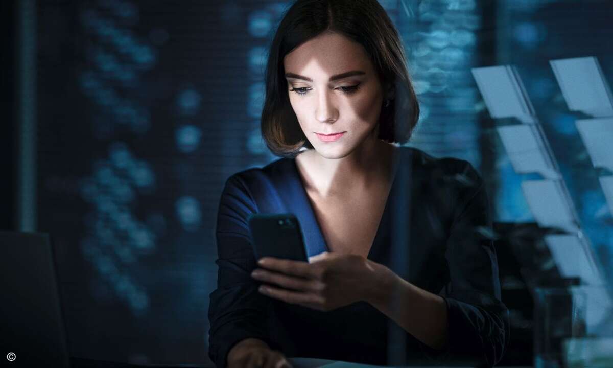 Attractive Female Manager Sitting at Her Table in Her Private Office and Using Smartphone. Behind Her is Window with Big City View.